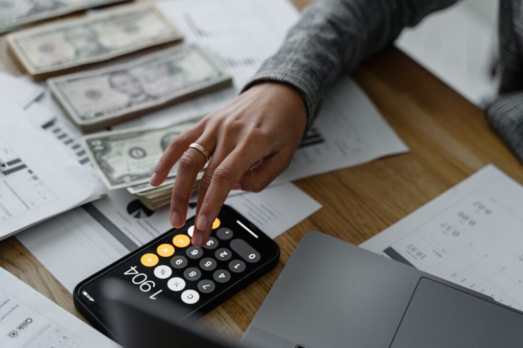 Close-up of a person using a budgeting app on their smartphone next to cash and financial documents