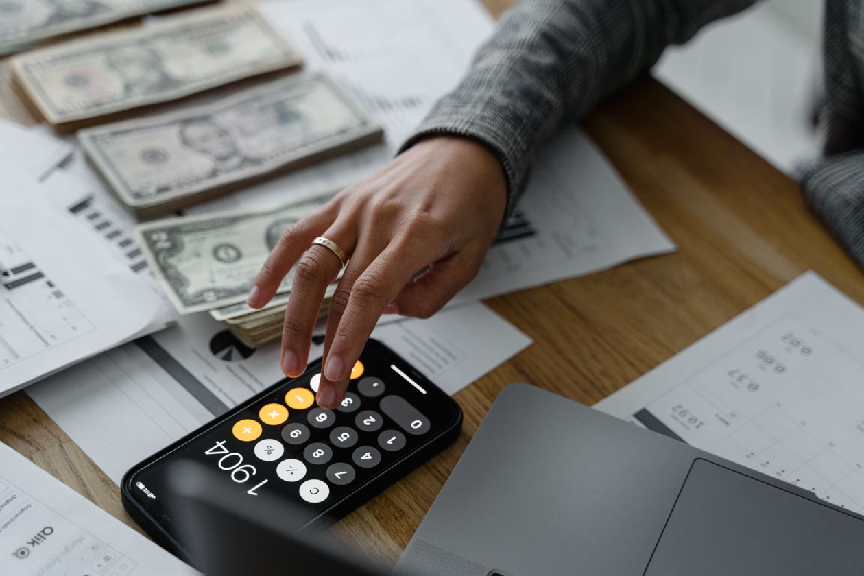Close-up of a person using a budgeting app on their smartphone next to cash and financial documents