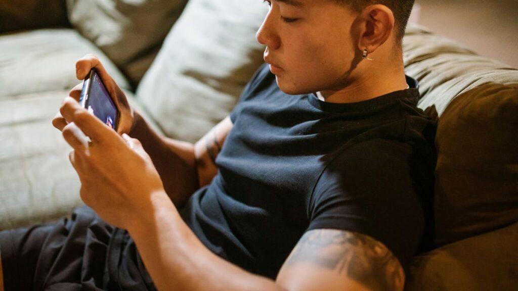 Young man playing a mobile battle royale game like BGMI on his smartphone at home