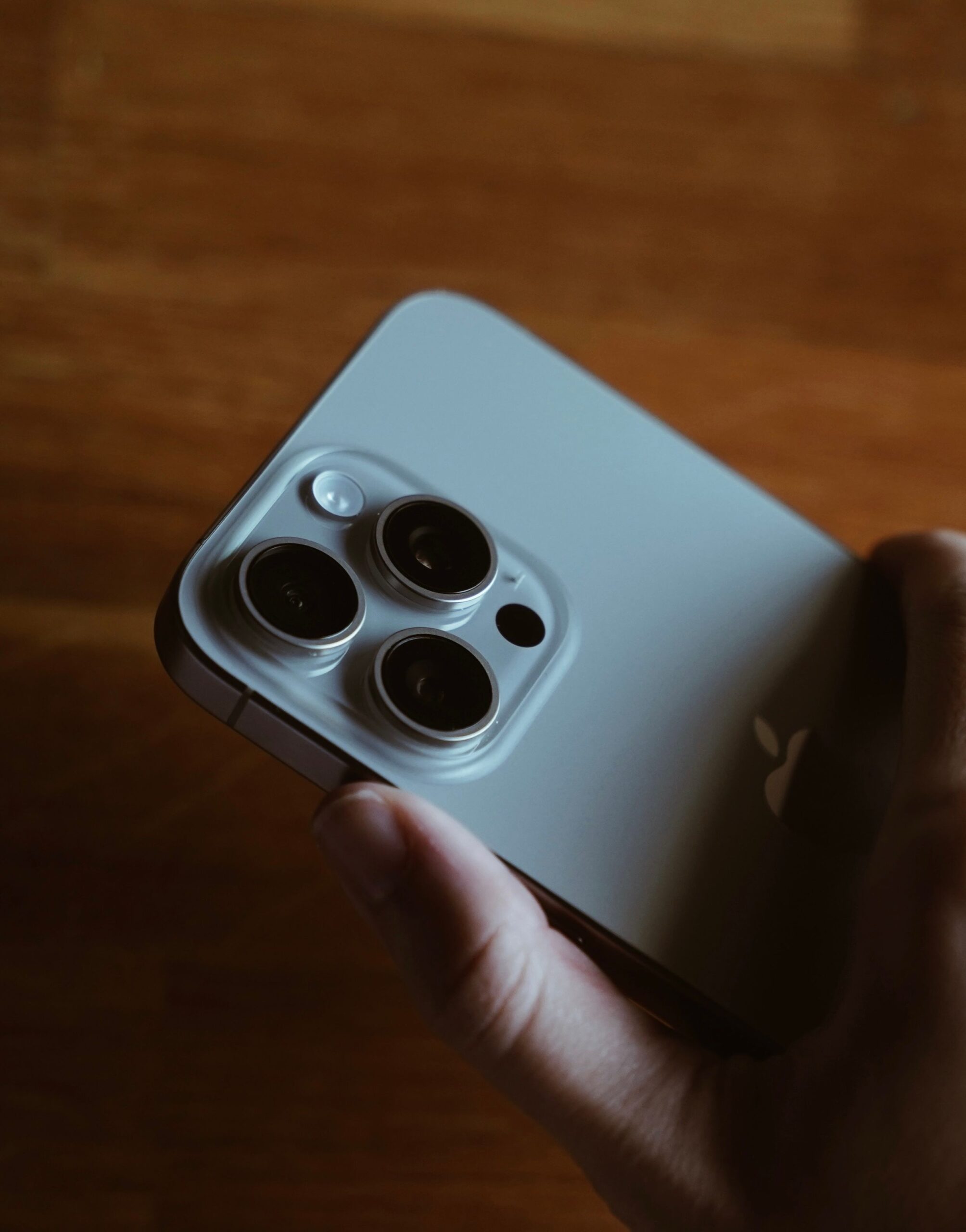 Hand holding a modern smartphone with triple camera lenses, representing the upcoming Apple iPhone 18 Pro Max design