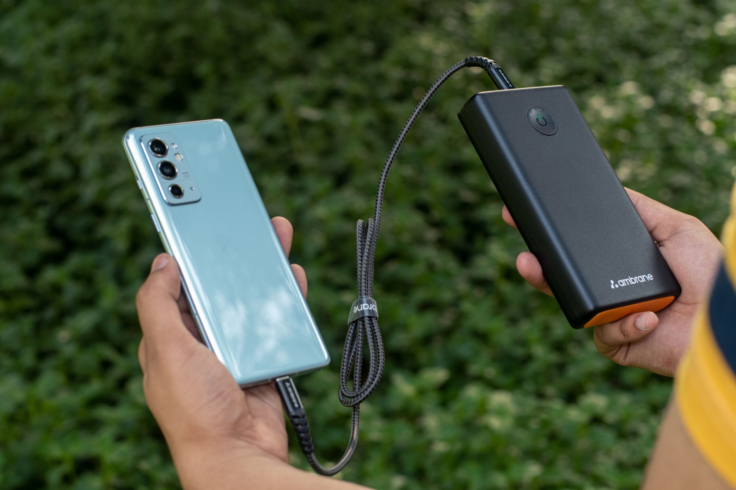 Hands holding a smartphone connected to a charging cable, representing the Nothing Phone 4b 33W fast charging and 6000mAh battery