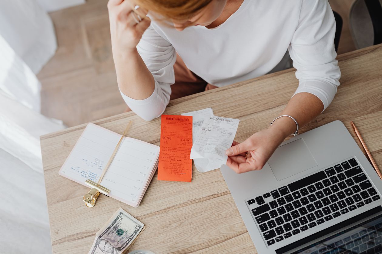 Woman reviewing monthly budget and expenses using a laptop and notebook at home