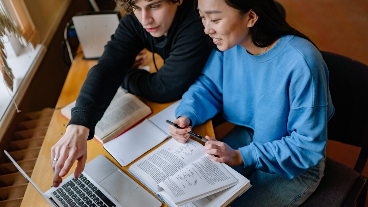 College students collaborating on a group study project using a laptop and textbooks