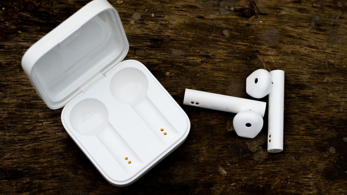 Close-up of white wireless earbuds and charging case on a wooden surface