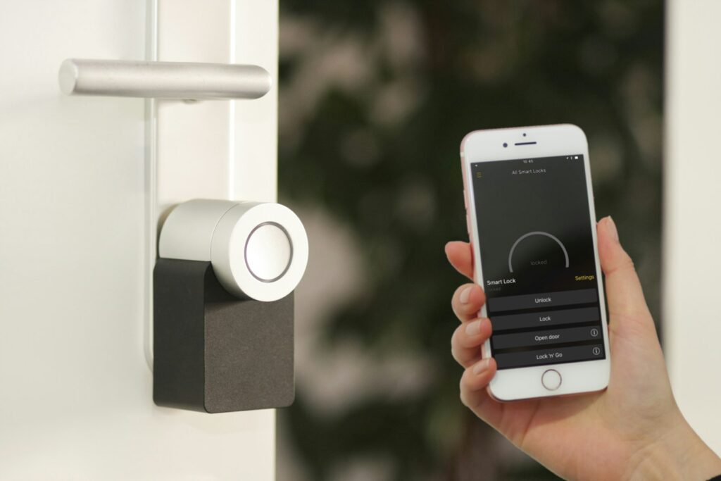 Smartphone held near a front door lock, representing app-controlled smart locks like August, Schlage, and Yale in the best smart locks 2026 comparison