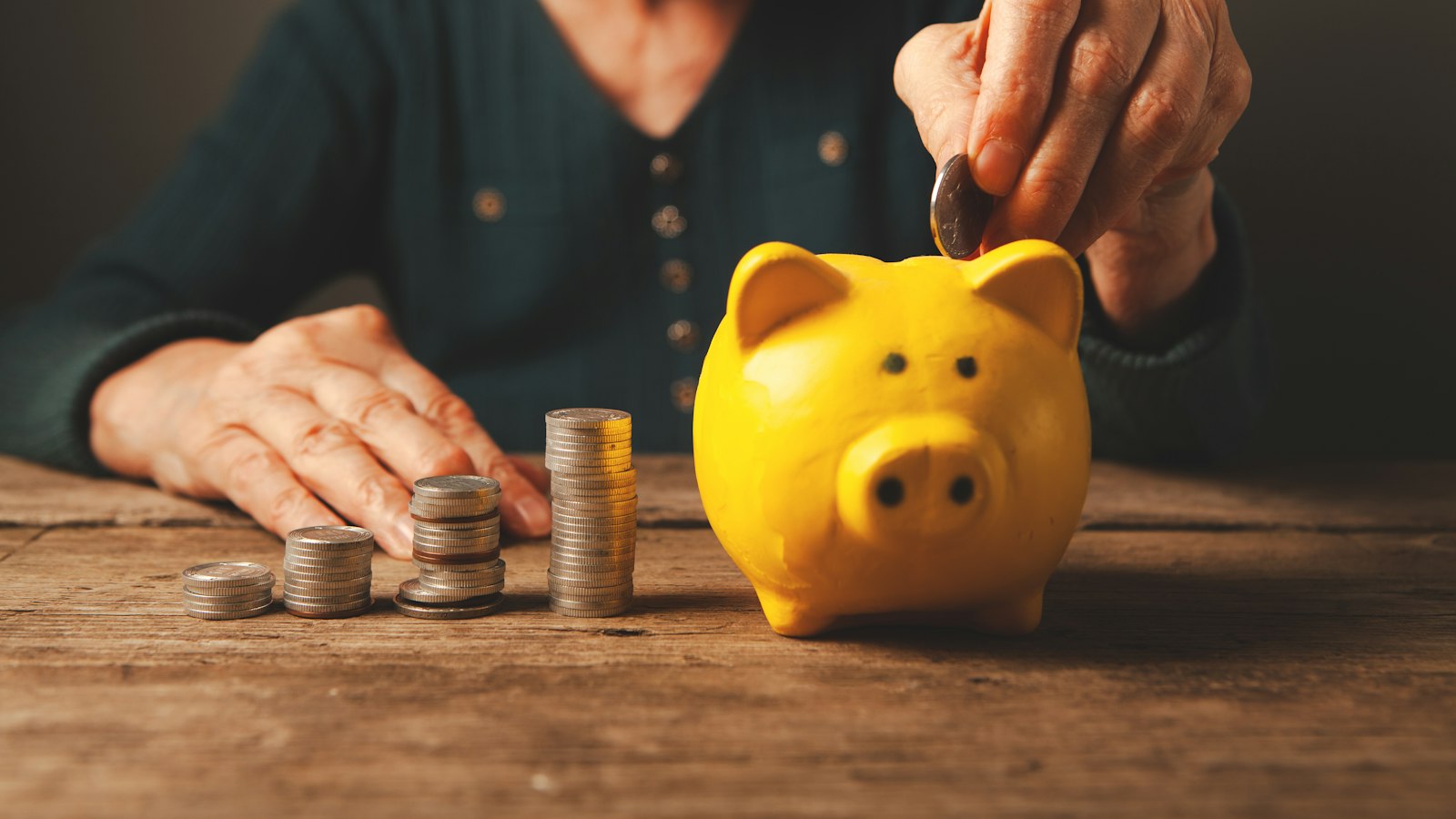 Elderly hands putting coins into a piggy bank, illustrating how much the Social Security COLA 2027 could add to monthly benefits